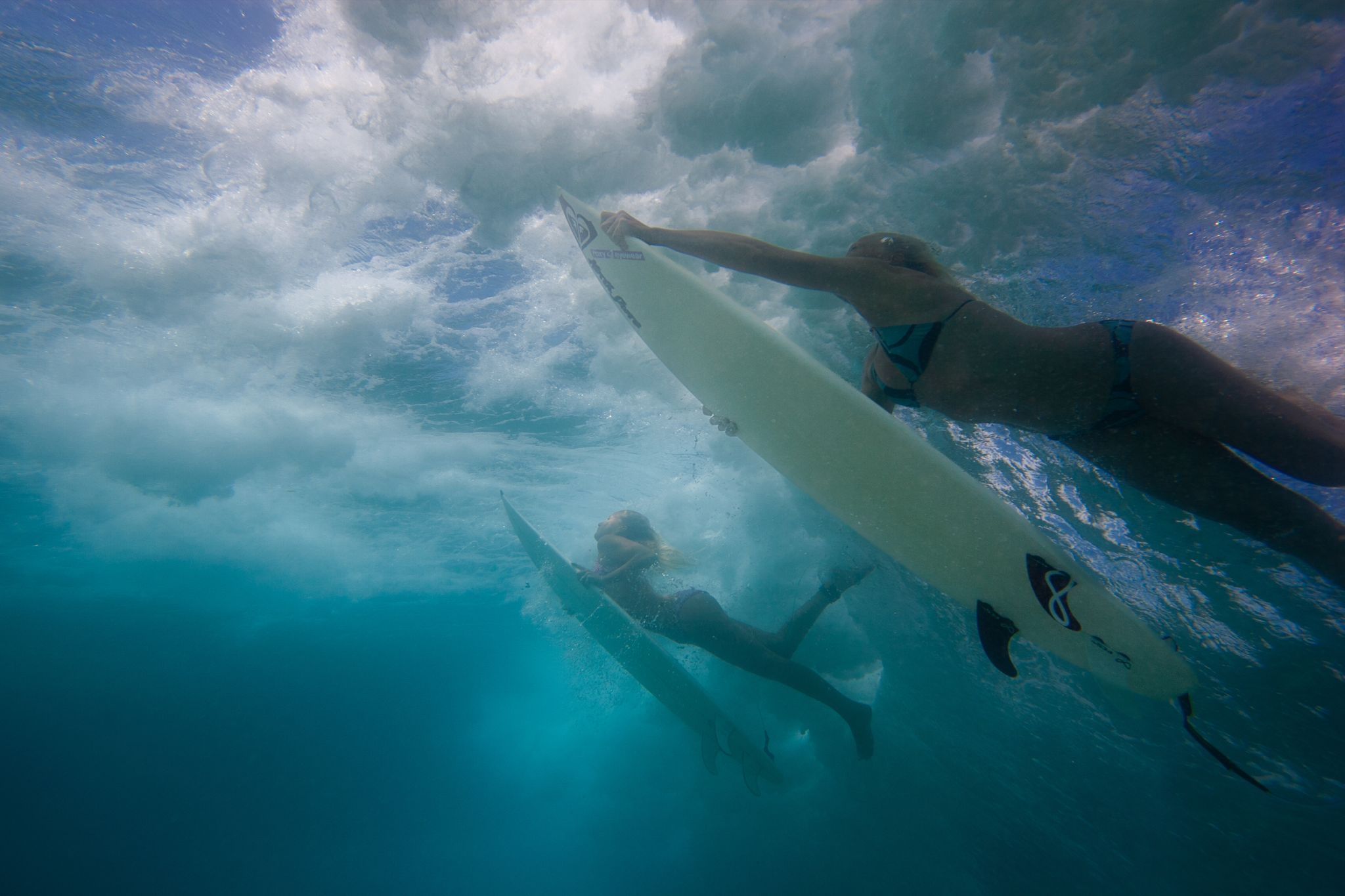 Zwei Surferinnen unter Wasser mit Surfbrettern.