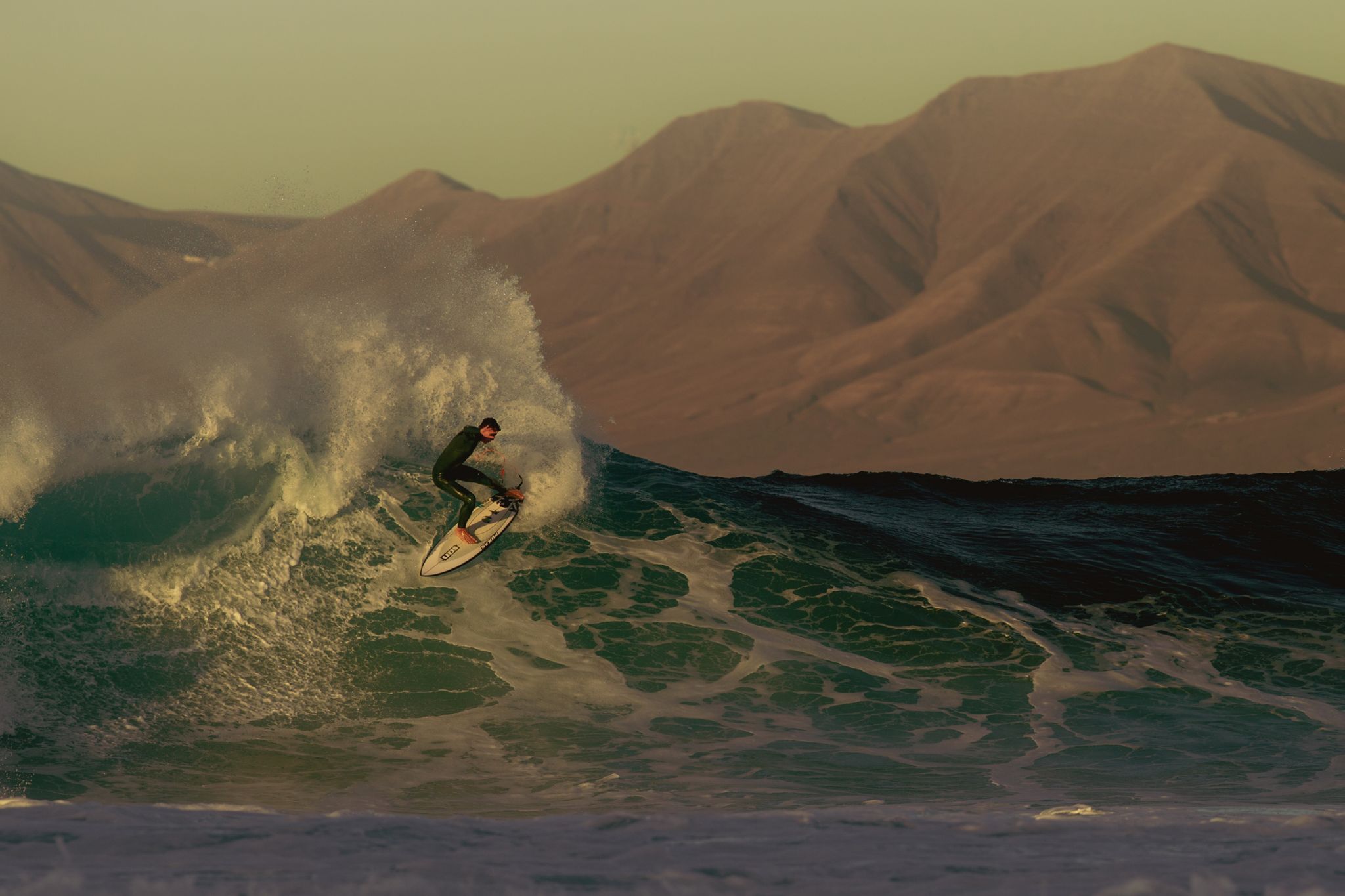 Surfer riding a wave with mountains in the background.