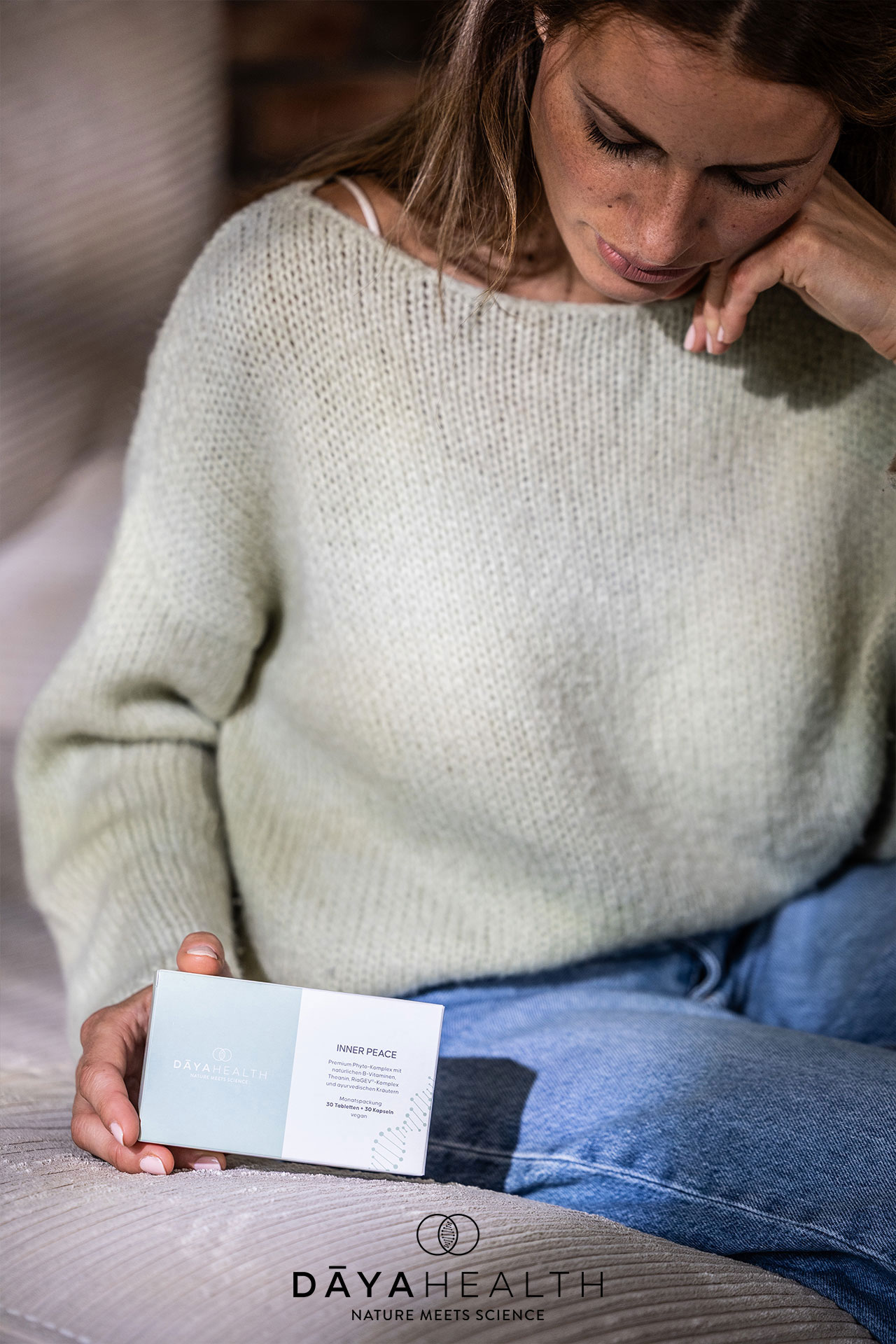 Frau mit Creme von DAYAHEALTH auf einer Couch.