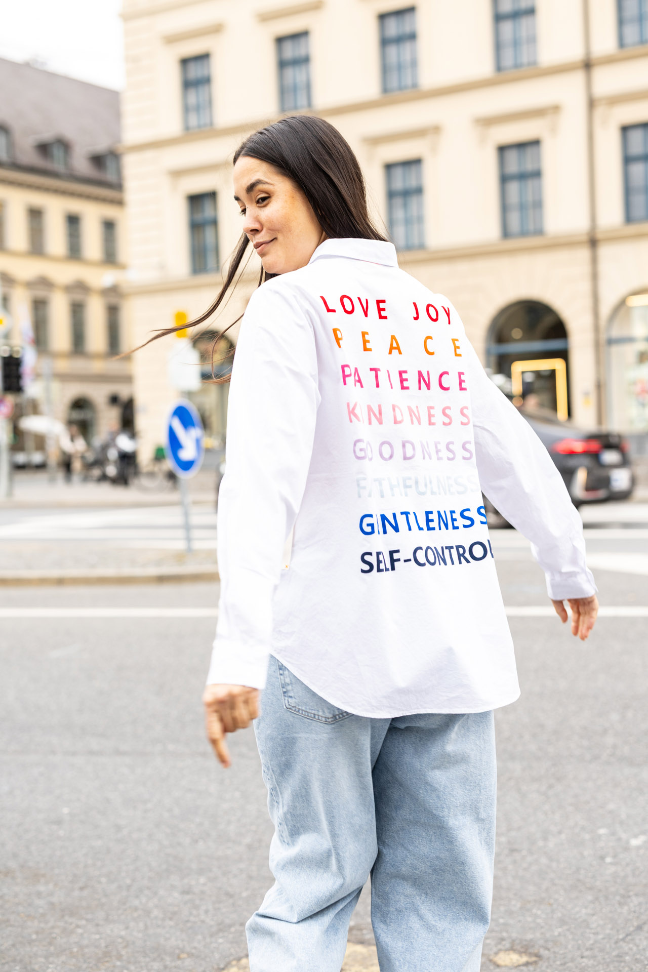 Eine lächelnde Frau in gestreiftem Pulli mit grauen Hosen, sitzt auf dem Boden.