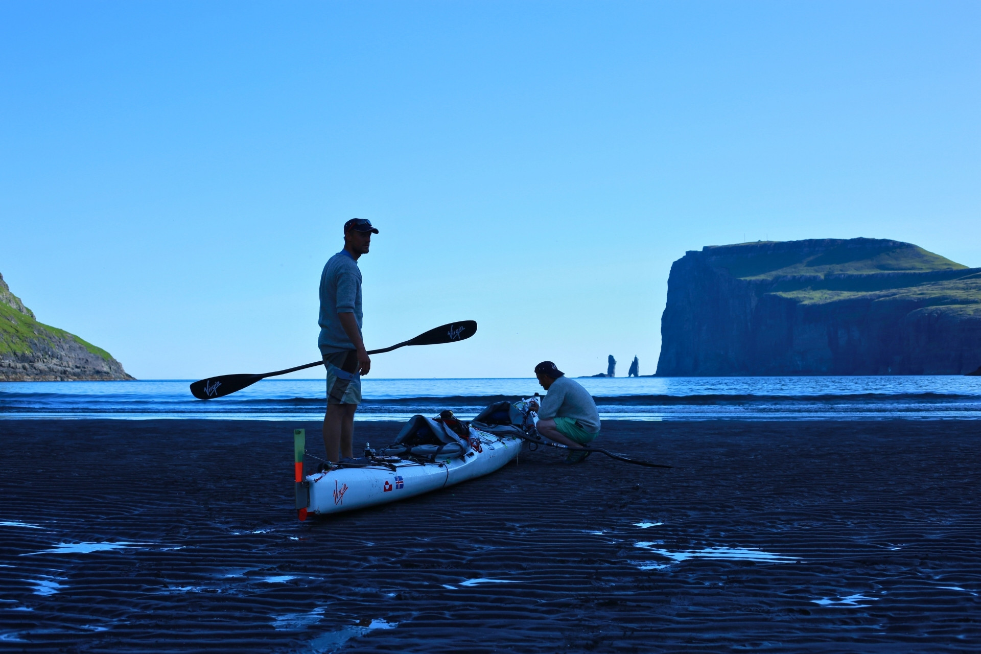Zwei Kajakfahrer am Strand mit Felsen im Hintergrund.