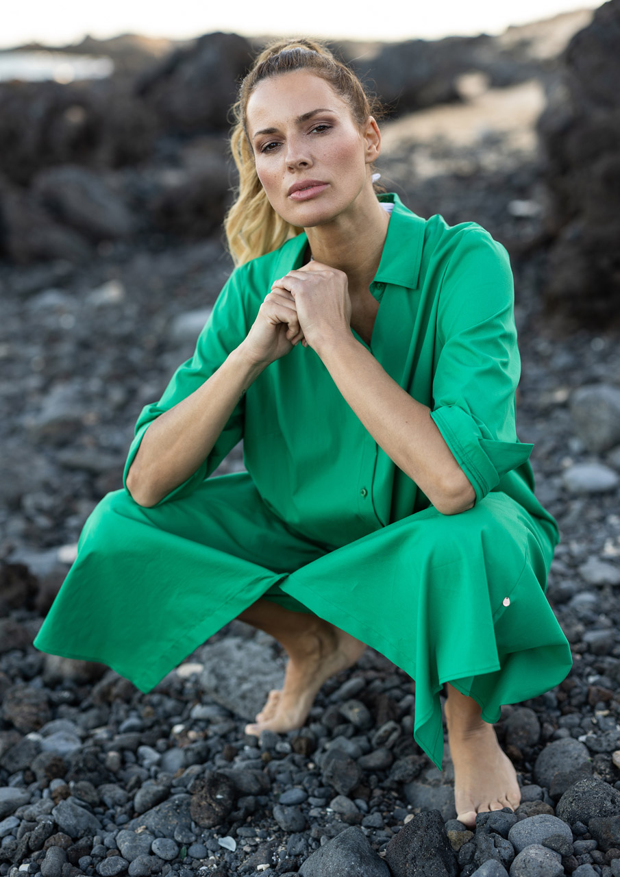 Frau in grünem Outfit, sitzt auf Steinen.