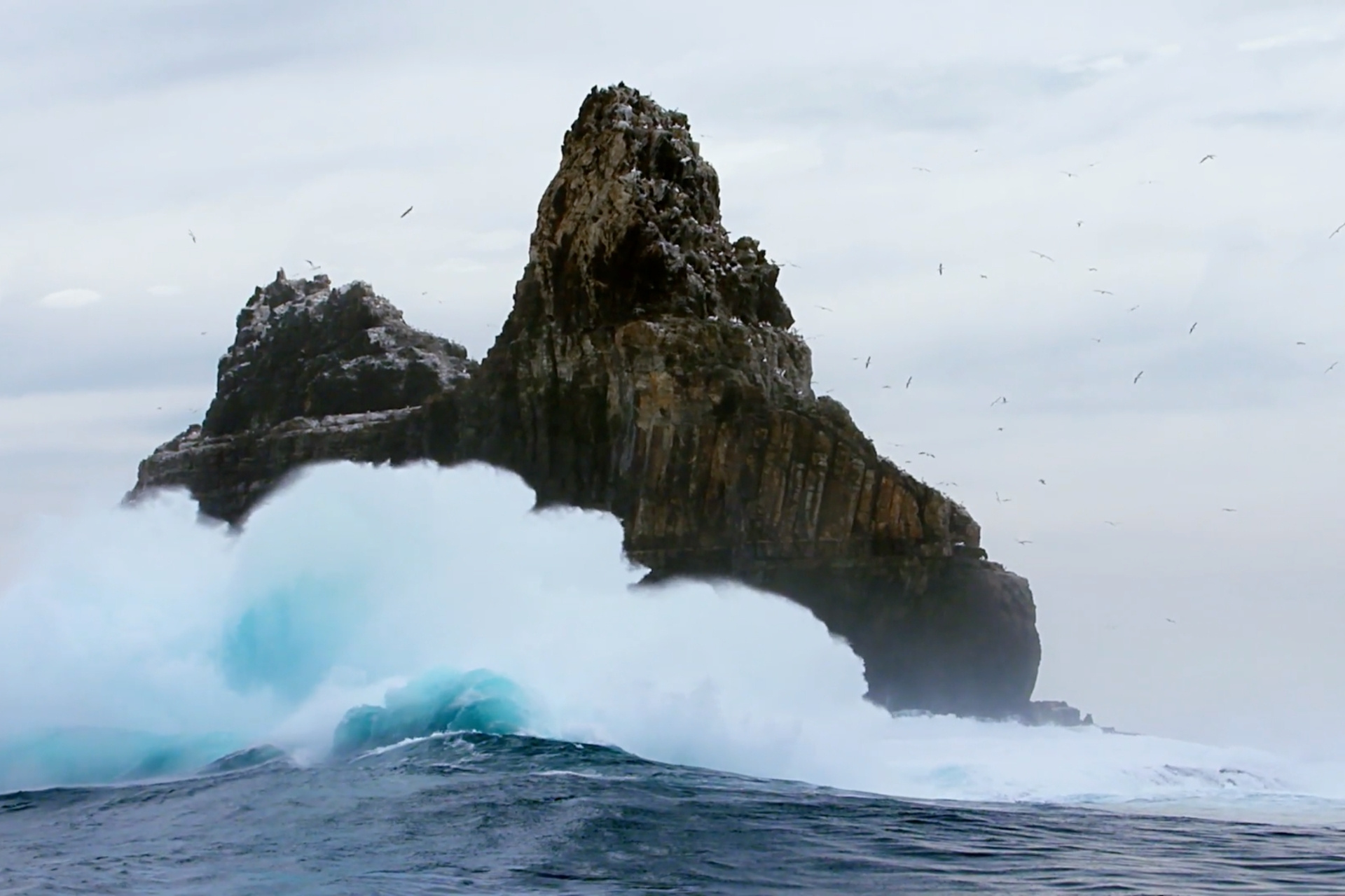 Wellen brechen gegen steile Klippe.