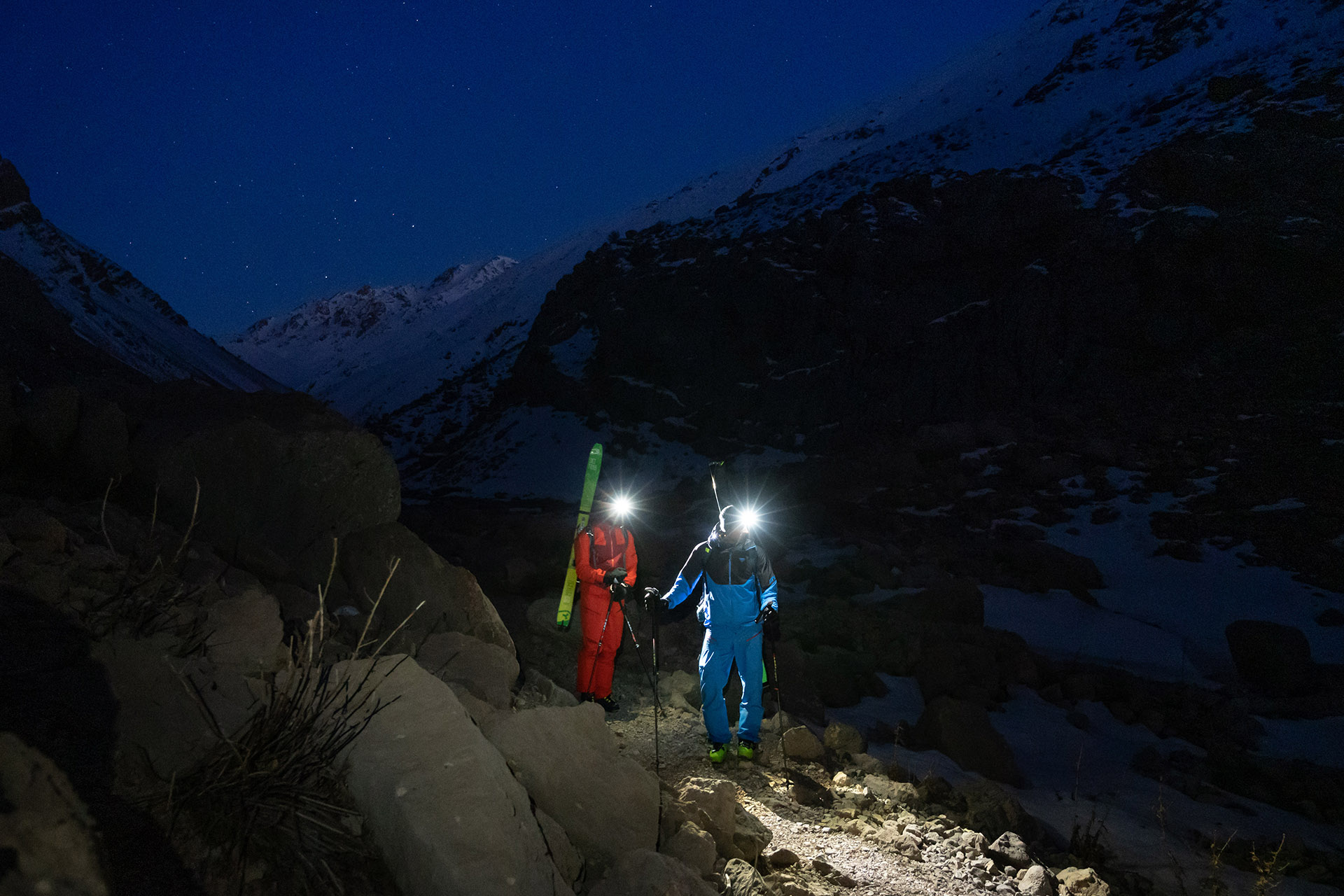 Zwei Skifahrer mit Stirnlampen auf einem nächtlichen Bergpfad.