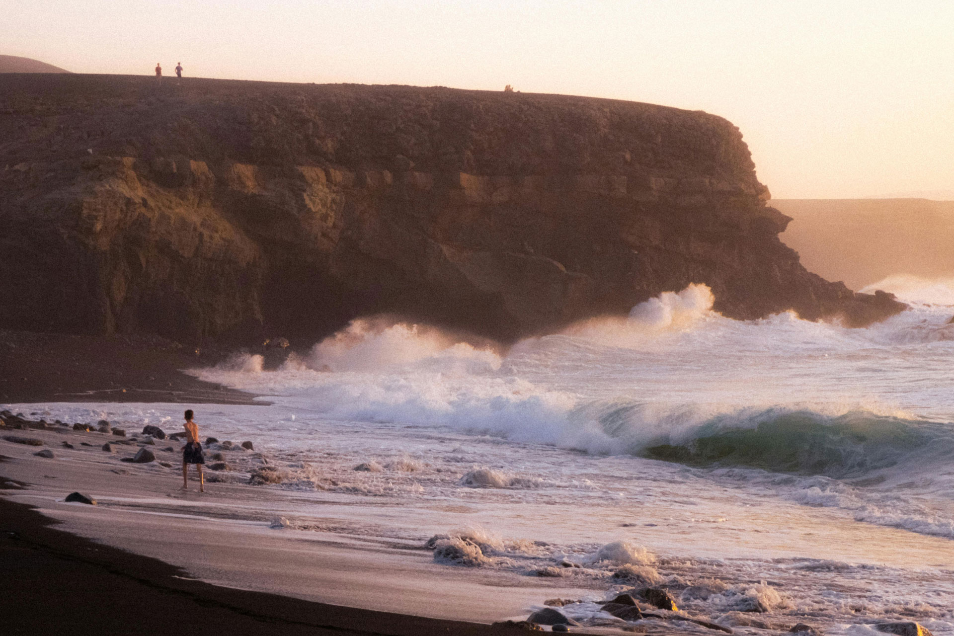 Person am Strand vor kliff mit Wellen.